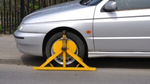 A yellow car boot clamped onto a gray car's tire.