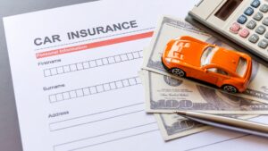 A car insurance form with an orange toy car, cash, and a calculator.