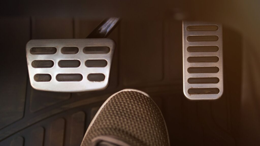 A gas and brake pedal with a foot in-between.
