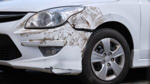 A white car with scratches and dents on the front bumper.