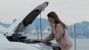 A woman on the phone while trying to figure out what is wrong with her car.