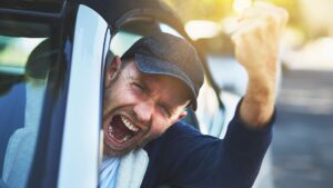 An angry man shaking his fist out the car window in anger.