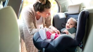 A mom putting their baby in a car seat in the back seat of her car.
