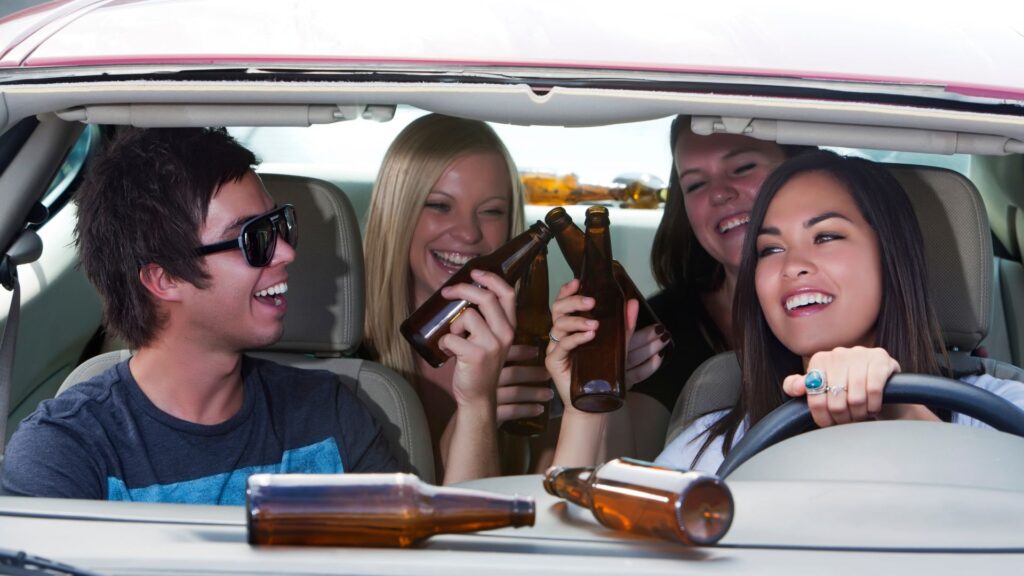 Three women and a man drinking alcohol in a car.