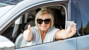 A old woman wearing sunglasses and is doing a thumbs up with her drivers license.