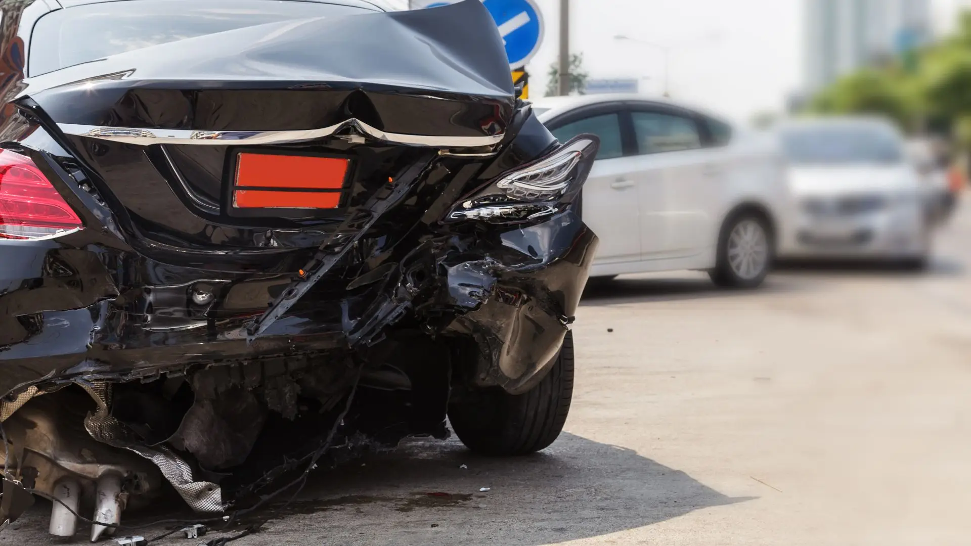 A black car that has a damaged rear bumper.