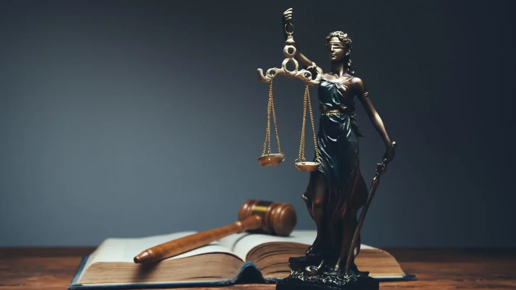 A small statue of lady justice, a book, and a gavel on a table.