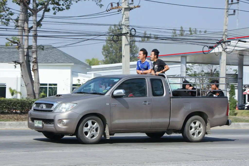Four people riding on the back of the truck while it is driving on the road.