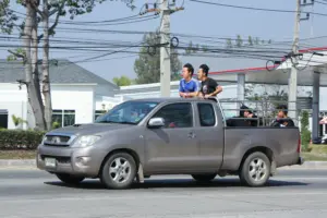Four people riding on the back of the truck while it is driving on the road.