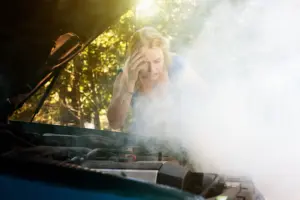A woman looking at the hood of her car as smoke is coming through.