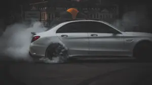 A gray car doing donuts in a middle of a street.